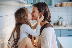 Mom kisses her little daughter in the kitchen photo