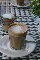 un café con leche en un vaso sobre una mesa en blanco y negro en un café al aire libre. foto