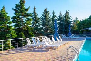 Primorsk, Ukraine. Poolside. Sunbeds near swimming pool surrounded by pine trees photo