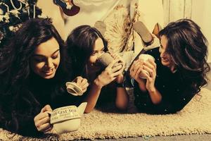 hermosa chica comiendo galletas de navidad y bebiendo té mientras está acostado en una alfombra. apartamento vintage decorativo. foto