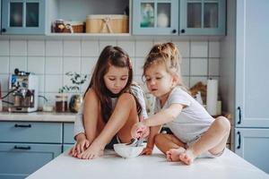 Two little girls in the kitchen sitting on the table. photo