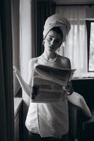 Beautiful young woman in a towel smokes a cigarette and reads newspaper photo