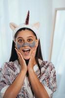 Woman applying facial mask on her face looks at the camera photo