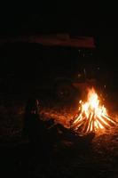 Woman sitting and getting warm near the bonfire in the night forest. photo