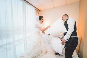Pillow fight of bride and groom in a hotel room photo