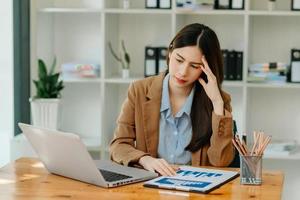 mujer que está cansada y pensando demasiado por trabajar con tableta y computadora portátil en la oficina moderna. foto