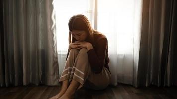 la mujer se sienta depresión de pie junto a la ventana y la ansiedad copia el espacio. foto