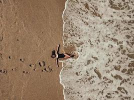 vista superior aérea joven tendida en la playa de arena y olas foto