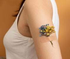 flor azul y amarilla debajo del parche en la mano de una mujer. el concepto de vacunación y tratamiento en ucrania