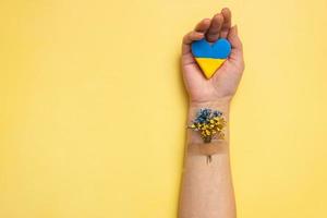 Blue and yellow heart and flowers under the patch on a female hand on yellow background. Treatment and recovery of Ukraine concept photo