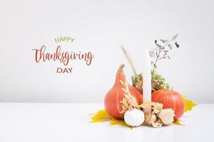 Autumn composition with Happy Thanksgiving Day greeting text. Dried leaves, pumpkins and candles on white background. photo