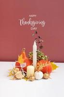 Autumn composition with Happy Thanksgiving Day greeting text. Dried leaves, pumpkins and candles on white pink background.