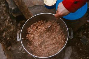 Camper preparing meal in large kettle on campfire photo