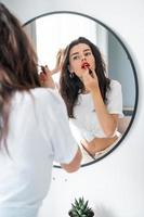 Young woman applying lipstick looking at mirror photo