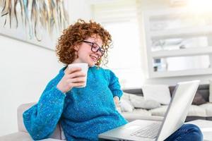 Nice beautiful lady with curly hair work at the notebook sit down on the sofa at home - check on oline shops for cyber monday sales - technology woman concept for alternative office freelance photo