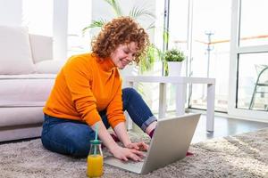 Creative female freelancer sitting front laptop computer and drinking an healthy orange juice. Freelance work Casual red hair woman working on computer while drinking orange juice photo