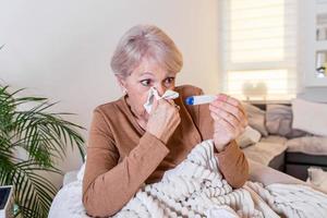 enfermedad, concepto de problema de coronavirus. anciana enferma con gripe tendida en el sofá mirando la temperatura en el termómetro. pandemia de COVID-19