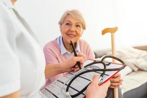 Senior woman is visited by her doctor or caregiver. Female doctor or nurse talking with senior patient. Medicine, age, health care and home care concept. Senior woman with her caregiver at home photo