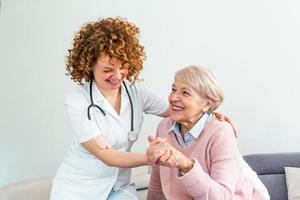 Young caring lovely caregiver and happy ward. Image of caregiver and senior resting in the living room. Smiling caregiver taking care of a happy elderly woman photo