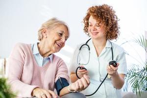 joven enfermera midiendo la presión arterial de una anciana en casa. enfermera controlando la presión arterial de una anciana en casa, cuidadora domiciliaria controlando la presión arterial de los pacientes foto