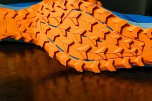 The soles of the two shoes were placed sideways on the black floor, Orange tread soles for trail running. The sole is very thick for wading on smooth roads and muddy roads. photo