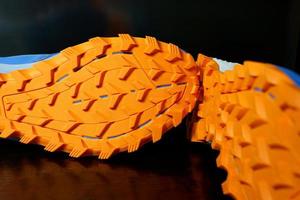 The soles of the two shoes were placed sideways on the black floor, Orange tread soles for trail running. The sole is very thick for wading on smooth roads and muddy roads. photo