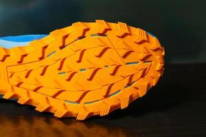 los zapatos se colocan sobre una superficie reflectante, suelas naranjas para trail running. la suela es muy gruesa para vadear por caminos llanos y caminos embarrados. foto