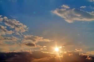 hermosa vista a los rayos de sol con algunas bengalas y nubes en un cielo azul foto