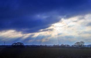 hermosa vista a los rayos de sol con algunas bengalas y nubes en un cielo azul foto