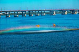 Athletes in kayaks in training near the river fountain in a rainbow of splashes. photo