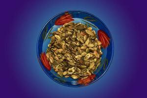 Peeled roasted pumpkin seeds in a glass blue bowl. Isolated macro photo close-up from above on a blue gradient