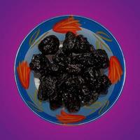 Dried black plums in a glass bowl. Isolated on purple gradient. Top view photo