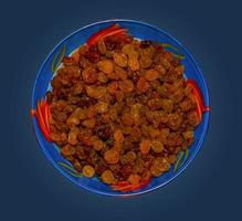 Raisins in a glass blue bowl. Isolated macro photo close-up from above on a black background