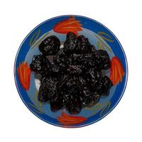 Dried black plums in glass bowl. Isolated on white background. Top view. photo