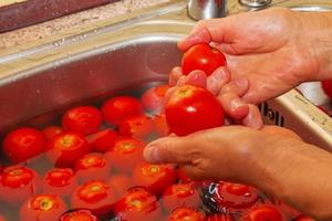 las manos de una mujer lavan los tomates con agua corriente en el fregadero de la cocina. foto