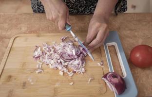 Top view of woman's hands chopping onion with a blue knife on a wooden board photo
