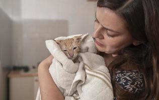 Close-up of a beautiful young Hispanic woman carefully drying her little light brown baby kitten with a white towel after having bathed her