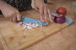 Close up of woman's hands chopping onion with a blue knife on a wooden board photo