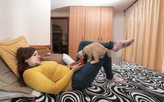 Beautiful Hispanic young woman lying on her bed playing with her little kitten with a red ball of yarn photo