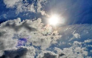 hermosa vista a los rayos de sol con algunas bengalas y nubes en un cielo azul foto