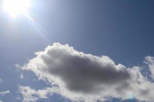 hermosa vista a los rayos de sol con algunas bengalas y nubes en un cielo azul foto