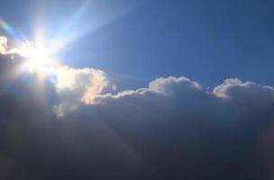 hermosa vista a los rayos de sol con algunas bengalas y nubes en un cielo azul foto