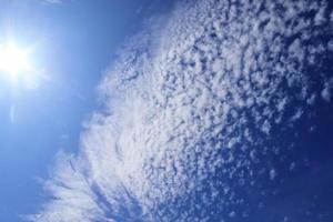 hermosa vista a los rayos de sol con algunas bengalas y nubes en un cielo azul foto