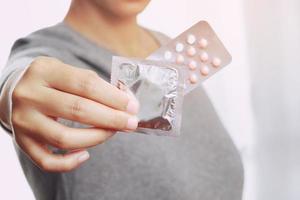 mano de mujer sosteniendo píldoras anticonceptivas y condones en la cama. protección, sexo seguro. concepto de control de la natalidad. copie el espacio foto