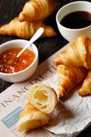 croissants recién horneados conjunto de deliciosos platos frescos en papel encerado sobre una mesa de madera oscura. desayuno francés espacio de copia de la vista superior. foto