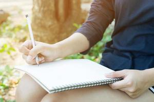 female hands with pen writing on notebook notepad sitting in public park outdoor. Leave copy space  empty write a message photo