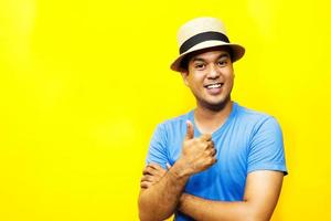 Portrait of cheerful asian man in basic clothing Casual wear hat smiling and show giving thumbs up at camera with showing success. isolated over yellow background. photo