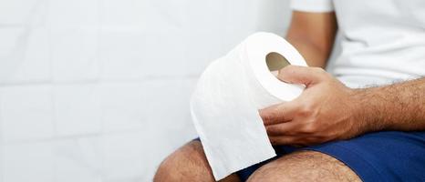 Man suffers from diarrhea hand hold tissue paper roll in front of toilet bowl. constipation in bathroom. Treatment stomach pain and Hygiene, health care photo