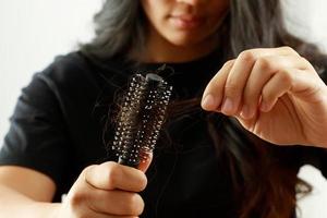 vista trasera mujer joven preocupada por el problema de pérdida de cabello, desequilibrio hormonal, concepto de estrés. muchos cabellos caen después de peinarse con un cepillo de pelo en la mano. mujer desenredó su cabello con un peine, cuidado de la salud foto