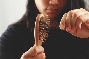 vista trasera mujer joven preocupada por el problema de pérdida de cabello, desequilibrio hormonal, concepto de estrés. muchos cabellos caen después de peinarse con un cepillo de pelo en la mano. mujer desenredó su cabello con un peine, cuidado de la salud foto